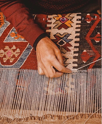 Hands weaving a rug